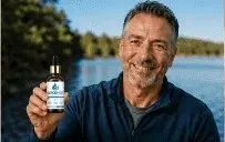 Smiling man holding GlycoMelt blood sugar support bottle outdoors near water